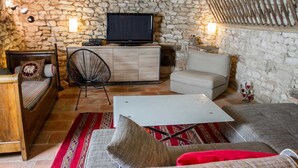 A cozy room with a stone wall, a television, a wooden bed, a chair, a sofa, and a small table. - The Yellow Crocodiles (CASTELNAU DE MONTMIRAL)