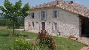 A stone house with a tiled roof, multiple windows with shutters, and a small garden area with plants and outdoor furniture. - The Yellow Crocodiles (CASTELNAU DE MONTMIRAL)