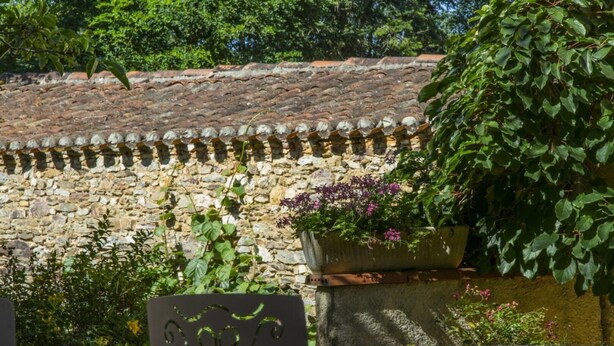 A stone wall with a tiled roof, a planter with flowers, and a metal sign.