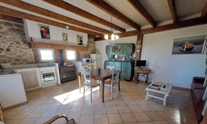 A kitchen with a dining area, stone wall, wooden beams, and a television.