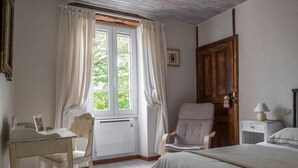 A bedroom with a bed, a chair, a desk, a wooden door, and a window with curtains.