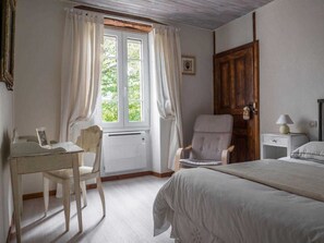 Un dormitorio con una cama, una silla, un escritorio, una puerta de madera y una ventana con cortinas.