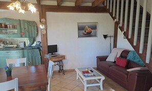 A living room with a dining table, a sofa, a television, and a kitchen area with a green cabinet.