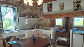 A kitchen with a stone wall, white cabinets, a wooden dining table, and a window.