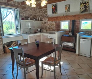 Una cocina con pared de piedra, armarios blancos, una mesa de comedor de madera y una ventana.