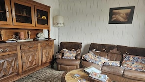 A living room with a brown leather sofa, patterned cushions, a wooden cabinet with glass doors, and a lamp. - Enjalbert - Albi - Gîte (Albi)