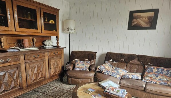 A living room with a brown leather sofa, patterned cushions, a wooden cabinet with glass doors, and a lamp.
