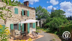 Un bâtiment en pierre avec des volets verts, des places assises à l’extérieur et un jardin.