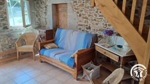 Une pièce au décor rustique, avec un canapé en bois, un fauteuil en osier et un bureau agrémenté d’un vase de fleurs.