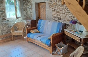 Une pièce au décor rustique, avec un canapé en bois, un fauteuil en osier et un bureau agrémenté d’un vase de fleurs.