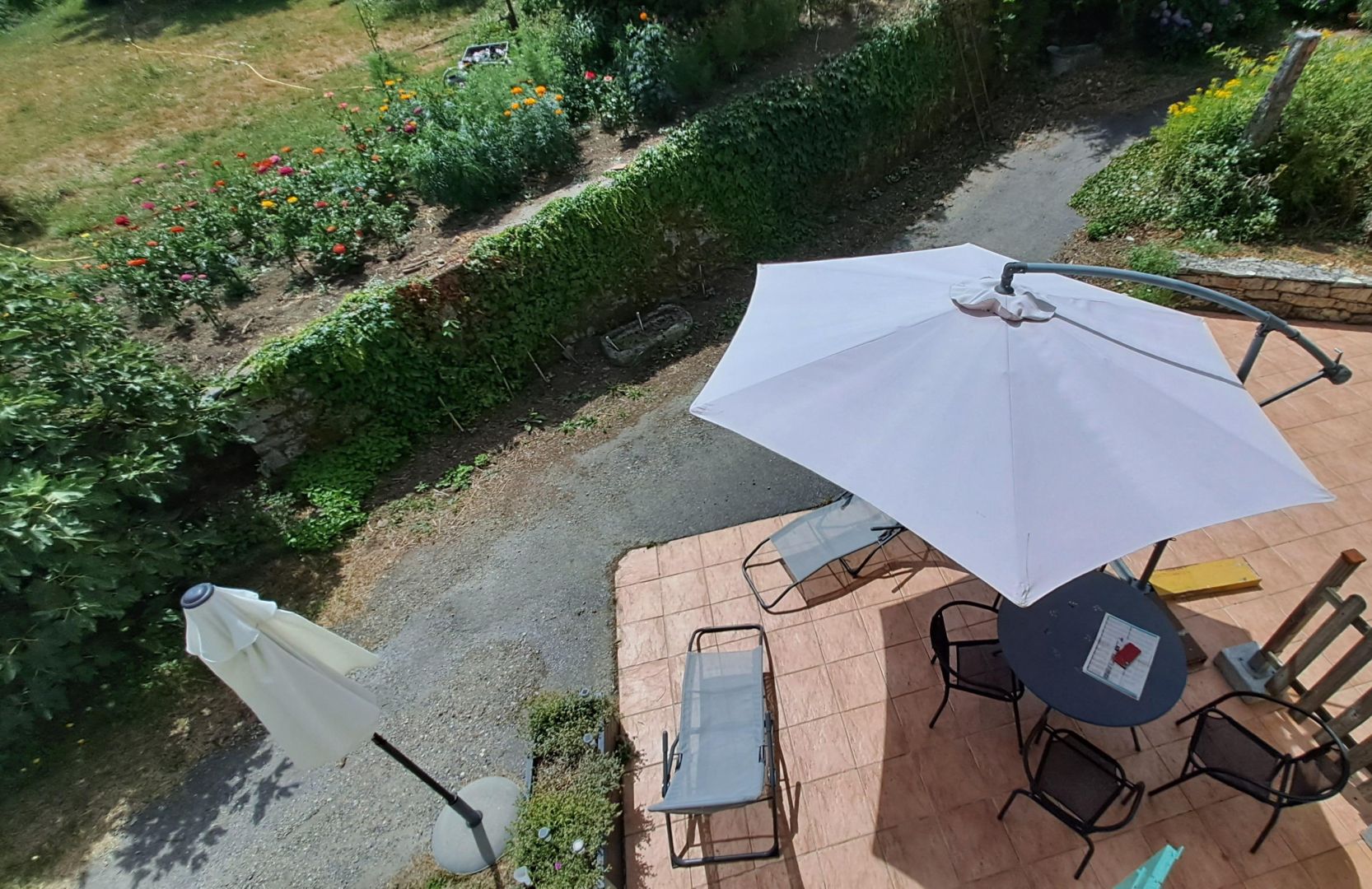 An outdoor patio with a table and chairs, a white umbrella, and a garden with flowers.