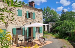 Un bâtiment en pierre avec des volets verts, des places assises à l’extérieur et un jardin.