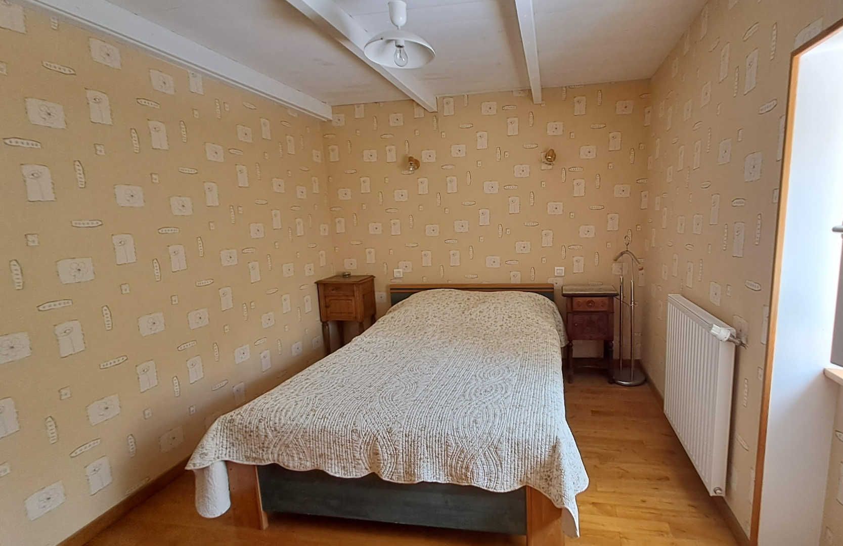 A bedroom with a bed, a nightstand, a radiator, and a window with curtains.