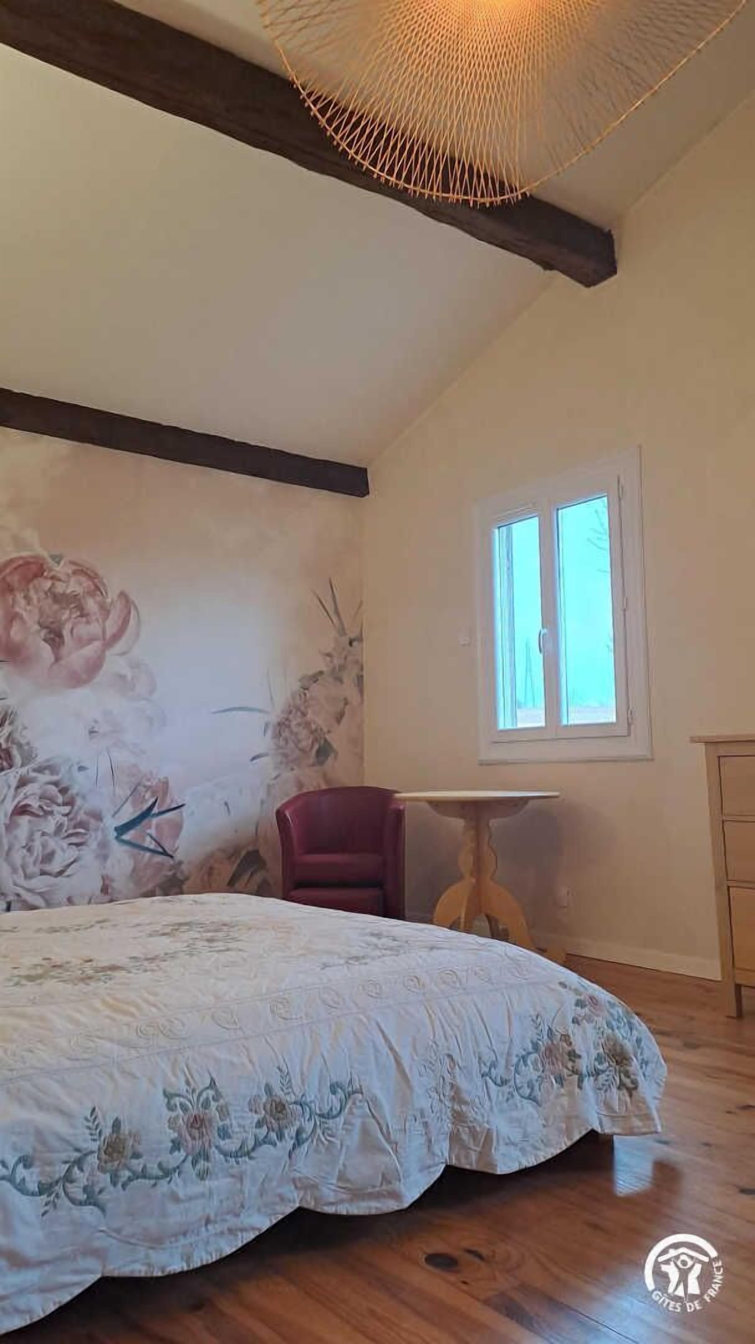 A bedroom with a large bed, a wooden ceiling, a window, and a chair.