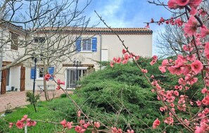 A two-story building with a tiled roof, a visible entrance, and a garden with blooming pink flowers.