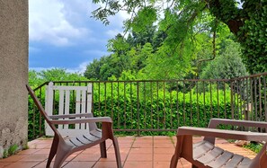 Ein Balkon mit zwei Holzstühlen, einem Metallgeländer und Blick auf einen üppigen Garten.