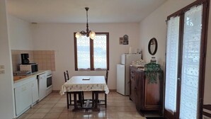 A kitchen with a dining table, chairs, a refrigerator, a microwave, and a coffee maker. - La Rivaillée - PARISOT (PARISOT)