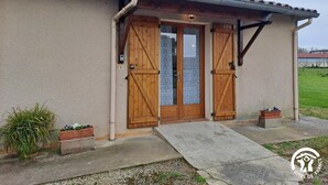 A house with a beige stucco exterior, a tiled roof, and a chimney. There are two wooden doors with glass panels, a small porch with a concrete step, and a metal antenna on the roof. - La Rivaillée - PARISOT (PARISOT)