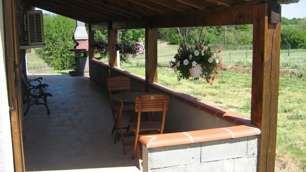 An outdoor patio with wooden chairs and a stone wall, overlooking a grassy field. - La Rivaillée - PARISOT (PARISOT)