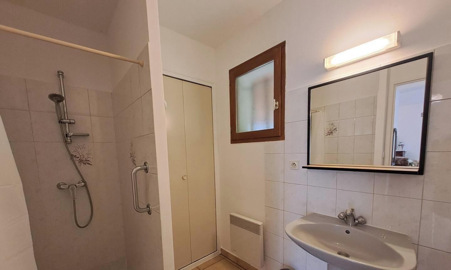Een badkamer met een douche, wastafel, spiegel en deur.
