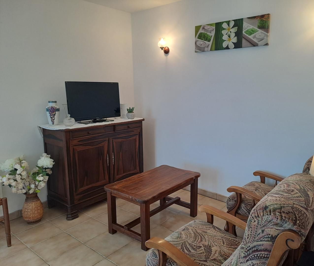 Een woonkamer met een televisie op een houten kast, een salontafel, gestreept fauteuils, een wandlamp en een schilderij.
