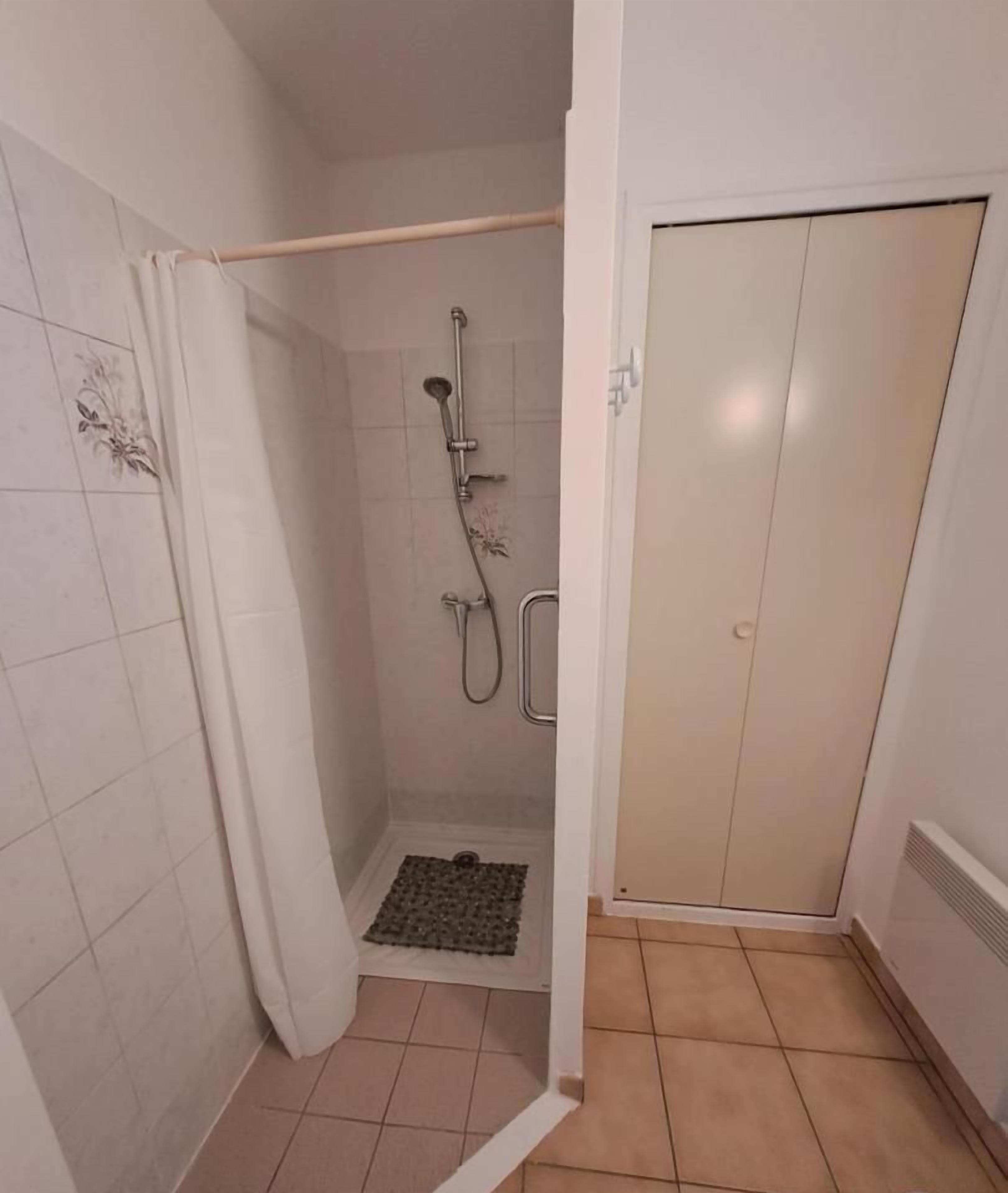 Un espacio de ducha pequeño y cerrado, con ducha, cabezal de ducha manual y rejilla de desagüe.