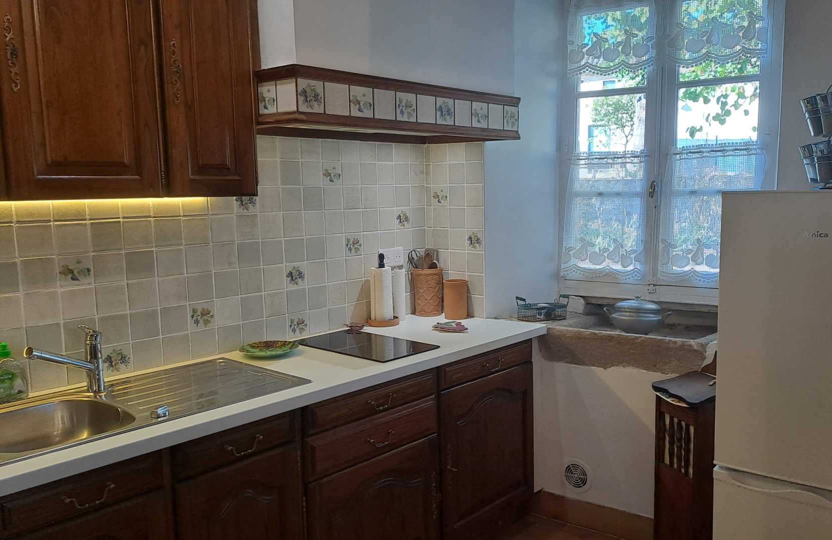 A kitchen with wooden cabinets, a white countertop, a sink, and a window with lace curtains.