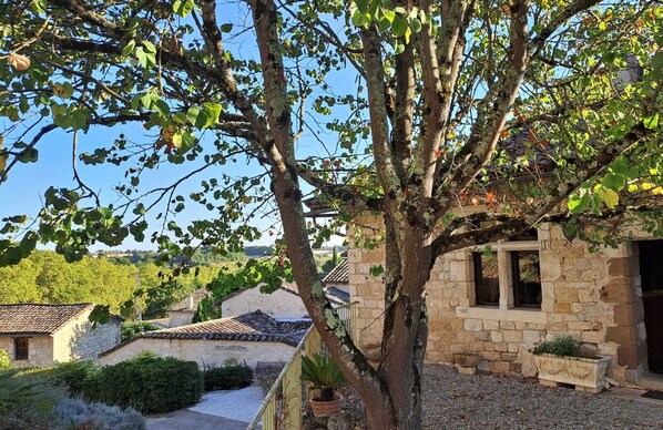 Un bâtiment en pierre avec un toit recouvert de tuiles, un arbre devant et un ciel dégagé.