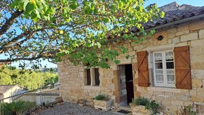 A stone house with wooden shutters, a gravel driveway, and a small garden area.