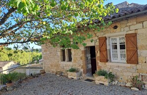 Une maison en pierre avec des volets en bois, une allée en gravier et un petit jardin.