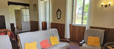 Un salon chaleureux avec un canapé et des fauteuils, des boiseries et une grande fenêtre.