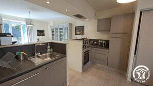 A modern kitchen with a central island, stainless steel appliances, and a view of the outdoors. - Le relais de la poste (CASTELNAU DE MONTMIRAL)