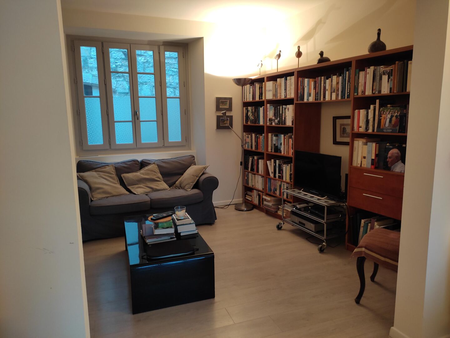 A living room with a sofa, coffee table, bookshelf, TV, and a window.