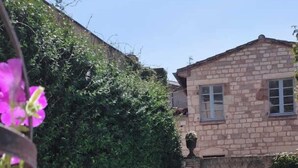 A swimming pool with clear blue water, surrounded by lush greenery and a stone building with windows. - Le relais de la poste (CASTELNAU DE MONTMIRAL)
