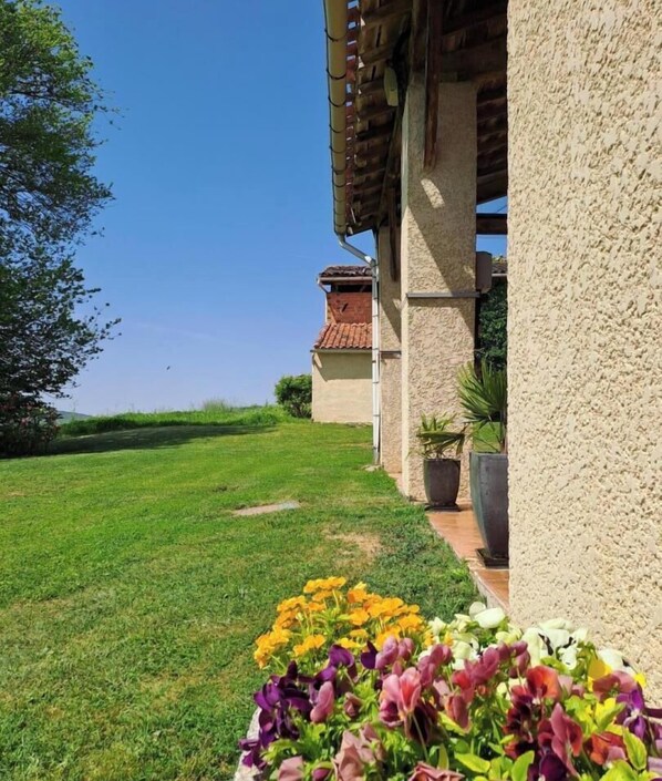A grassy area with a building, a clear sky, and a flower bed.