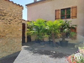 A courtyard with stone walls, potted plants, and a building with wooden shutters.