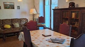 A dining area with a table set for four, surrounded by chairs. There is a sofa and a lamp in the background. - Les Bons Enfants - VENES (VENES)