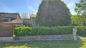 A residential area with a large tree, a fenced yard, and a building with a tiled roof. - Les Bons Enfants - VENES (VENES)