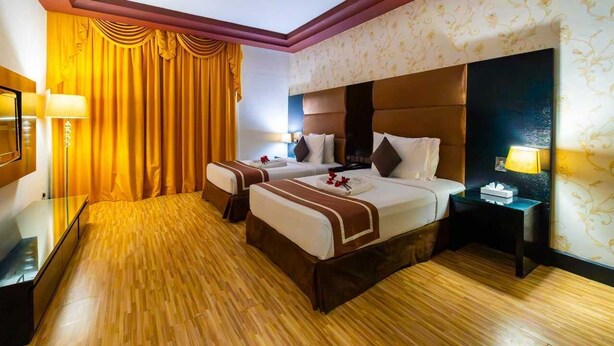 Une chambre d’hôtel avec deux lits, un plancher en bois, une grande fenêtre avec des rideaux et une table de chevet avec une lampe.
