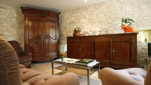 A living room with a stone wall, a wooden cabinet, a sofa, a coffee table, and a television. - Saint Martial - Terre de Bancalié (Terre de Bancalié)