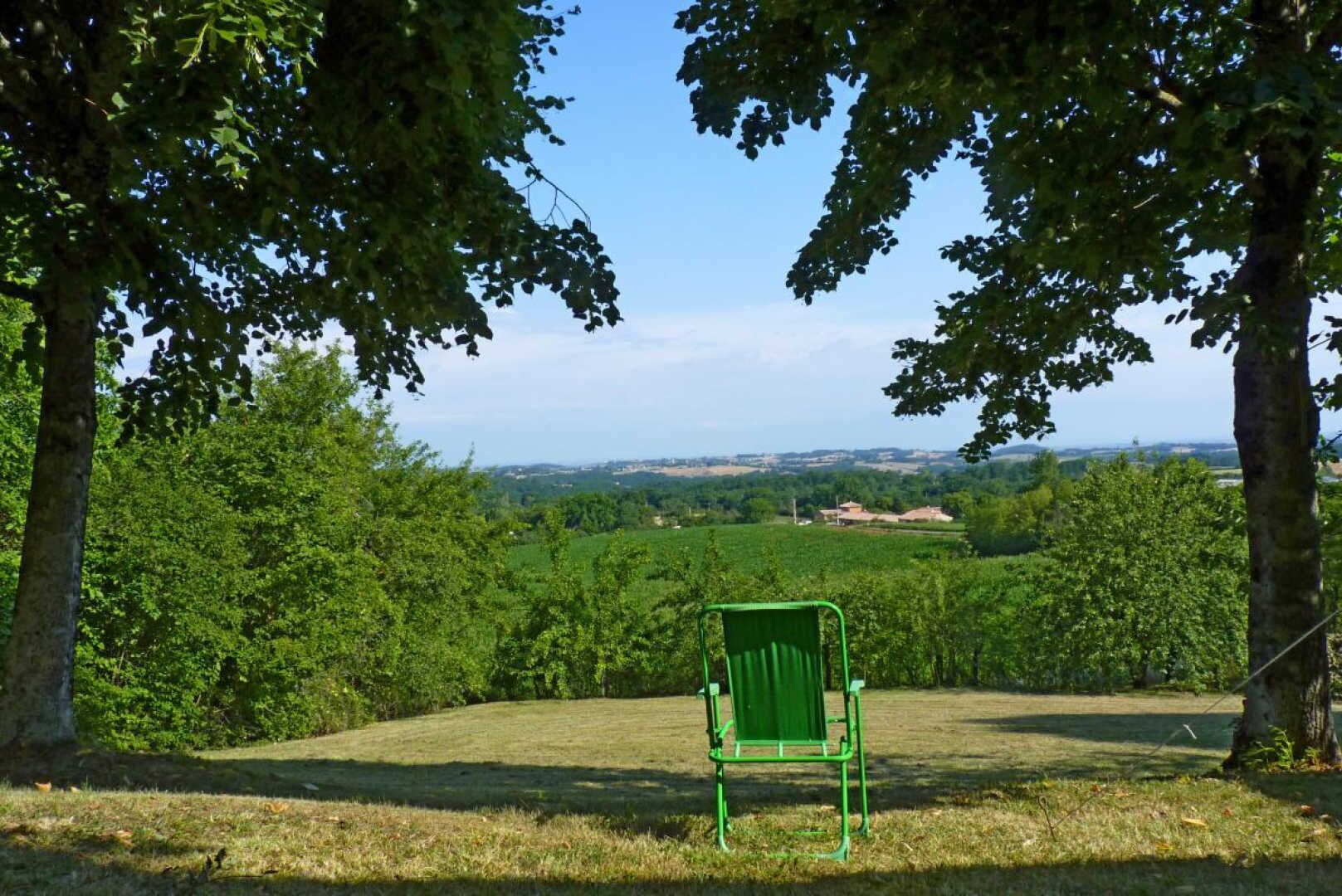 Een groene stoel in een begrazend veld met bomen en een uitgestrekt landschap in de verte.