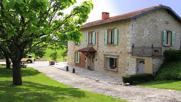 Une maison en pierre avec des volets verts, un balcon et une allée pavée.