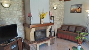 A living room with a stone wall, a fireplace, a sofa, a TV, and a potted plant. - La Teulière - LOMBERS - Gîte (LOMBERS)