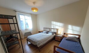 A bedroom with a bunk bed, a single bed, a bedside table with a lamp, and a hanging light fixture.