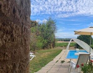 Ett poolområde med utsikt över vingårdar, en pergola och en stol med en röd ros.