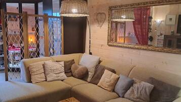 Een gezellige woonkamer met een hoekbank, twee hangende rieten lampen en een grote spiegel aan de muur.