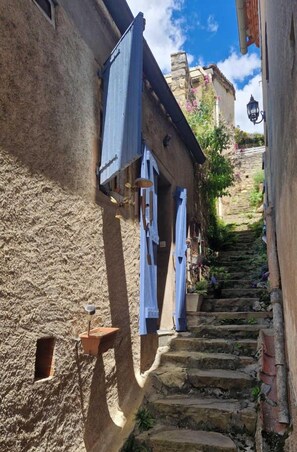 A narrow stone staircase in a historic town with wooden shutters on the buildings.
