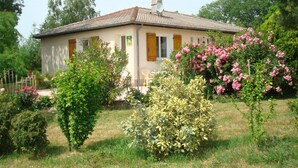 A single-story house with a tiled roof, surrounded by lush greenery and flowering plants. - Les Barreaux - MONTVALEN (MONTVALEN)