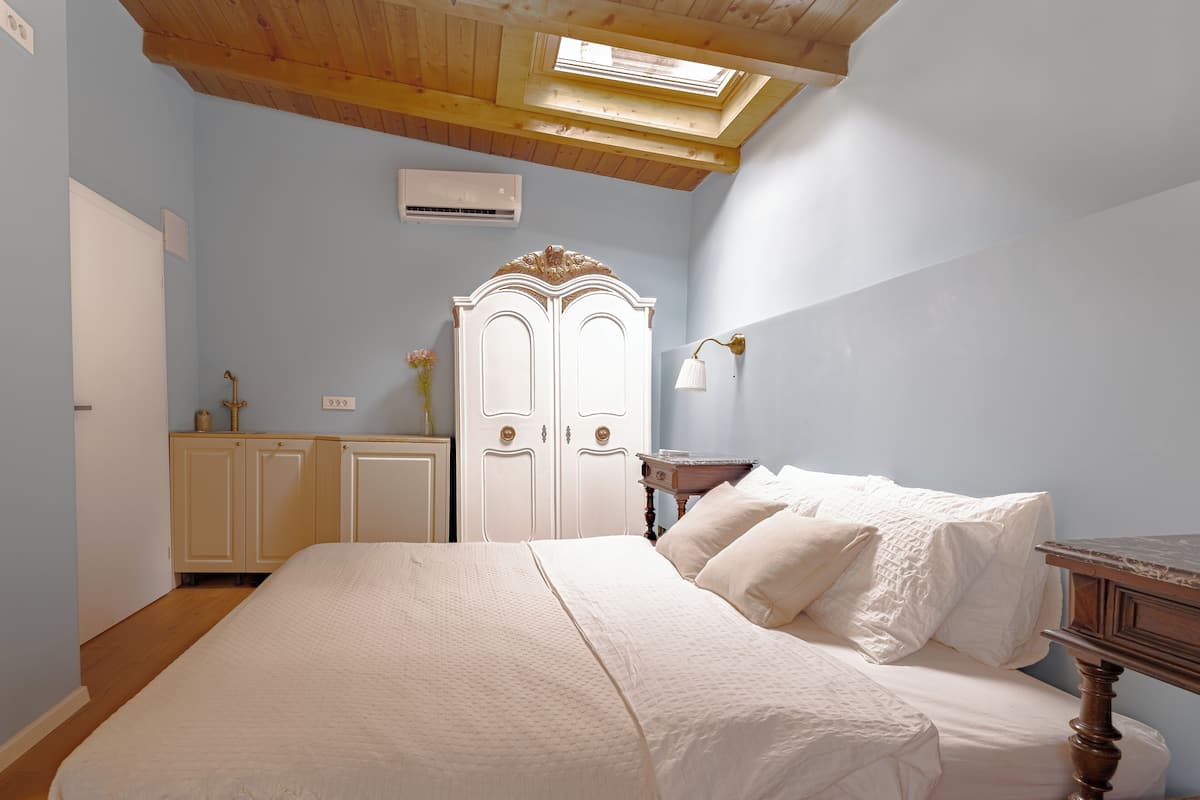 A bedroom with a bed, a wardrobe, an air conditioning unit, and a skylight.