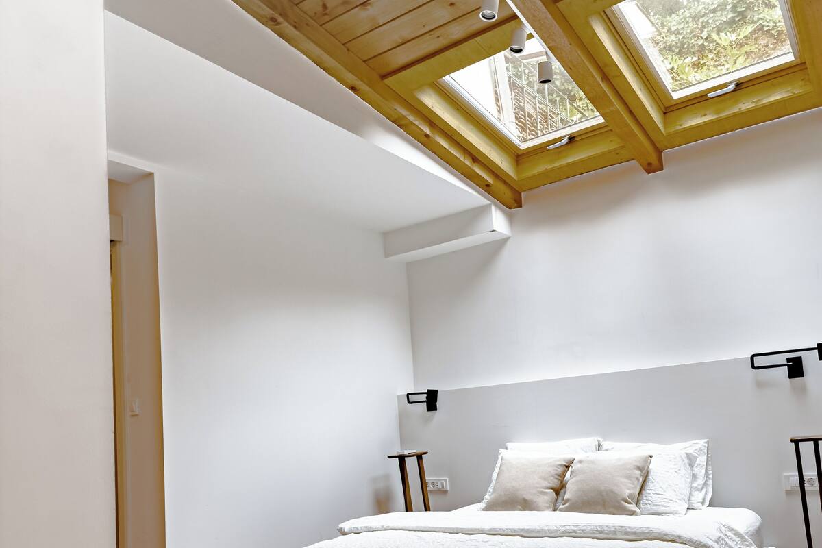 A bedroom with a bed, skylights, white walls, and wooden flooring.
